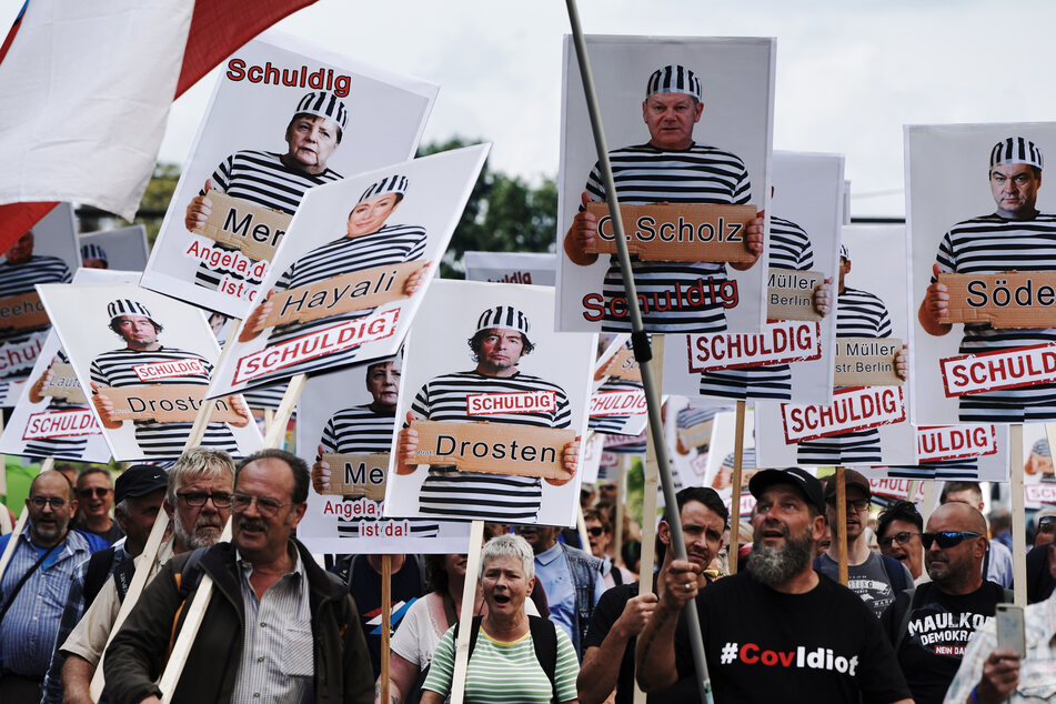 Teilnehmer einer Demonstration gegen die Corona-Maßnahmen halten Schilder mit Fotos von Politikern, Journalisten und Wissenschaftlern jeweils mit Namen und "Schuldig".