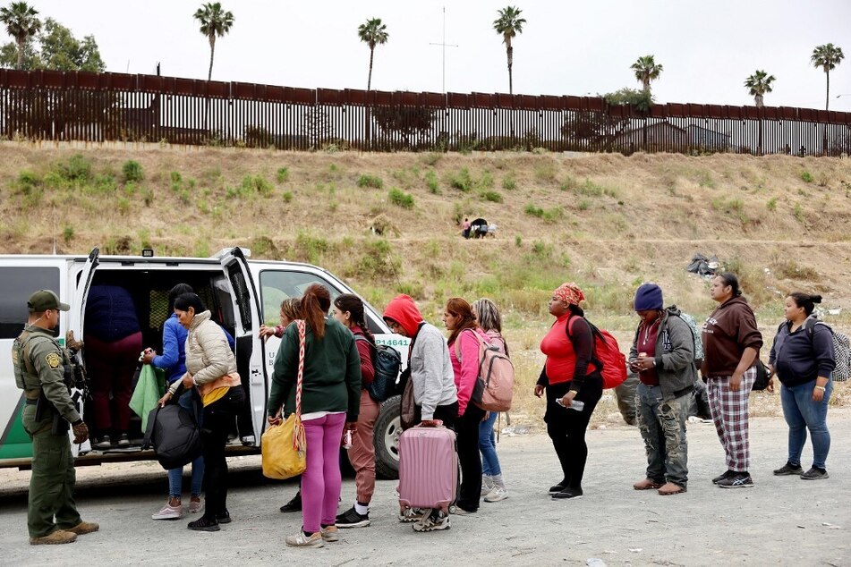 A US Border Patrol agent keeps watch as immigrants enter a vehicle to be transported from a makeshift camp near the US-Mexico border.