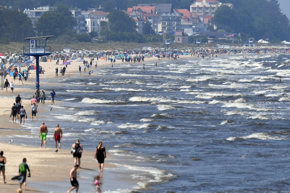 Touristen spazieren am Strand an der Ostsee auf der Insel Usedom entlang. Millionen Urlauber in Deutschland fahren jedes Jahr ans Meer.