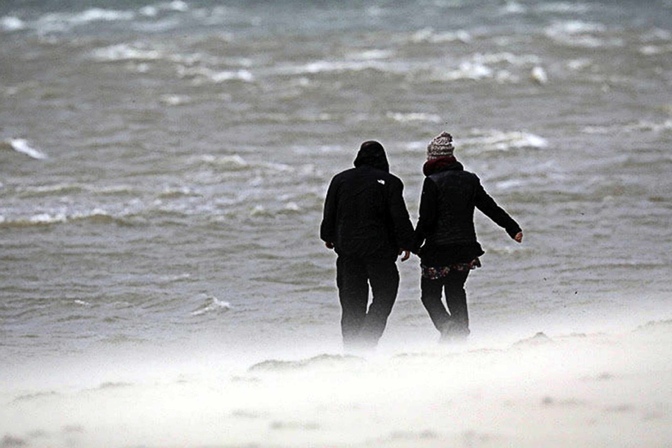 Zwei Urlauber gehen bei Sturm am Strand spazieren. (Archivbild)