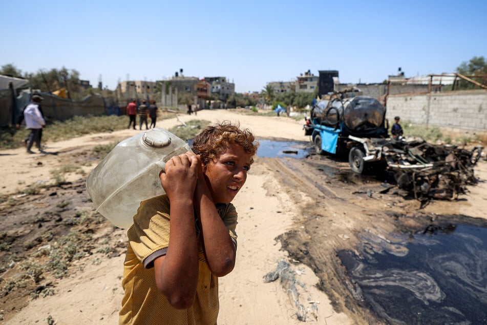 A boy carries a jerrycan filled with water drawn from the tank of a destroyed mobile water cistern that was hit by Israeli bombardment in the Nuseirat camp for Palestinian refugees in the central Gaza Strip on July 14, 2025.
