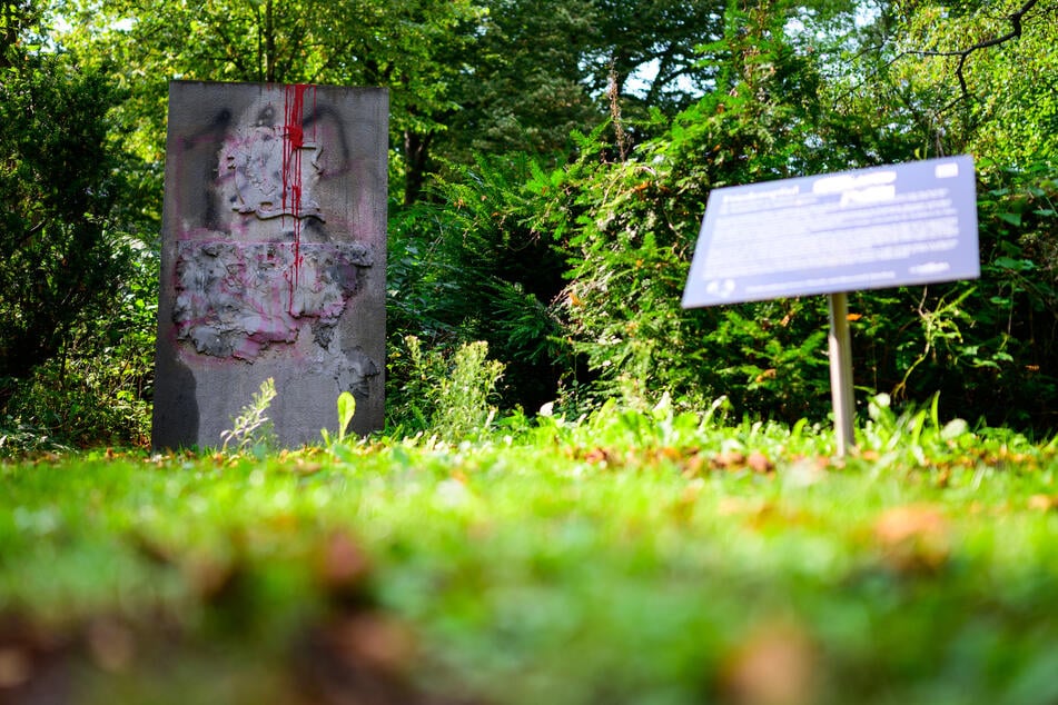 Das Denkmal und die Erläuterungstafel stehen in einer Grünanlage in Lüneburg.