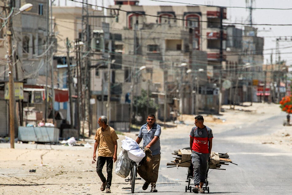 A man pulls a cart loaded with salvaged wood alongside another pushing a bicycle loaded with bags along a street in the eastern part of Rafah in the southern Gaza Strip on June 14.