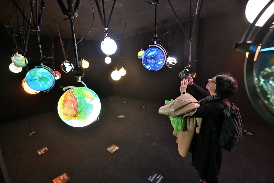 Ingo Günther lässt illuminierte Globen in einem dunklen Raum von der Decke hängen, um unterschiedlichste Daten zu visualisieren.