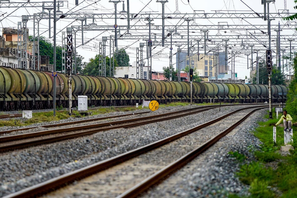 A man sits by railway tracks as a freight train transports petrol wagons in Ajmer, India, on August 27, 2025.