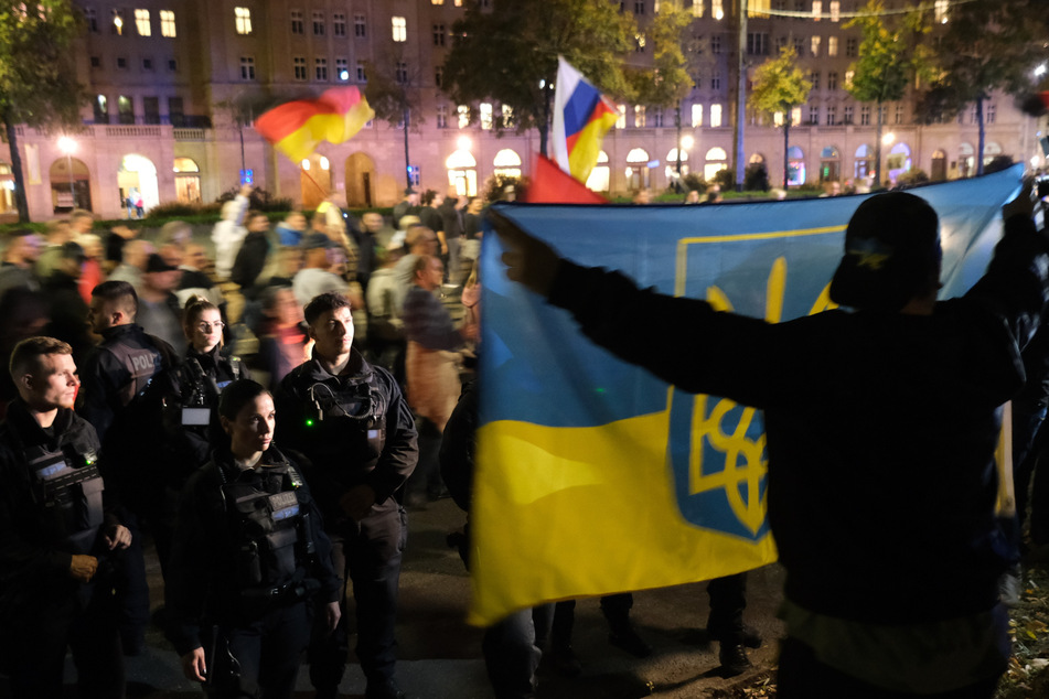 Teilnehmer einer Demonstration in Leipzig gehen mit Fahnen eine Straße entlang, während ein Gegendemonstrant im Vordergrund eine ukrainische Fahne hält.