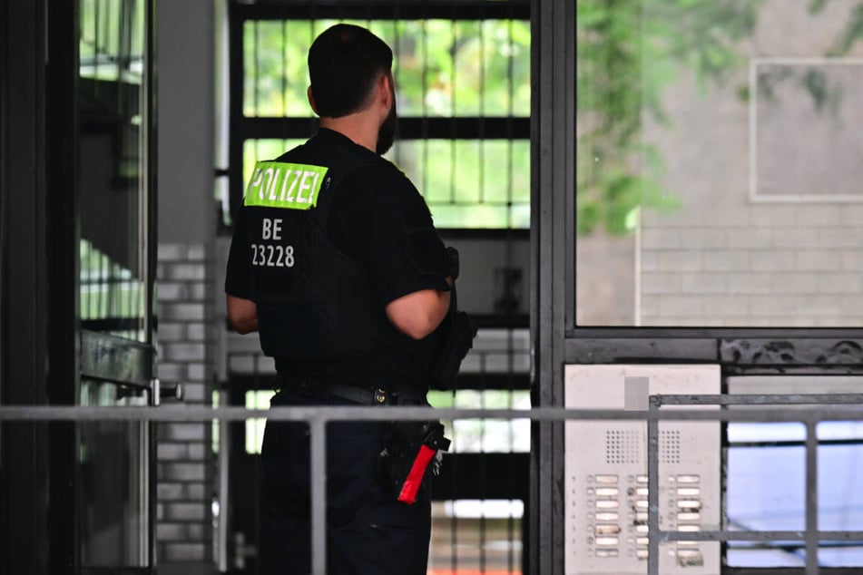 Ein Polizist steht im Hauseingang des Wohnblocks, in dem in der Nacht eine Wohnung durchsucht worden ist.