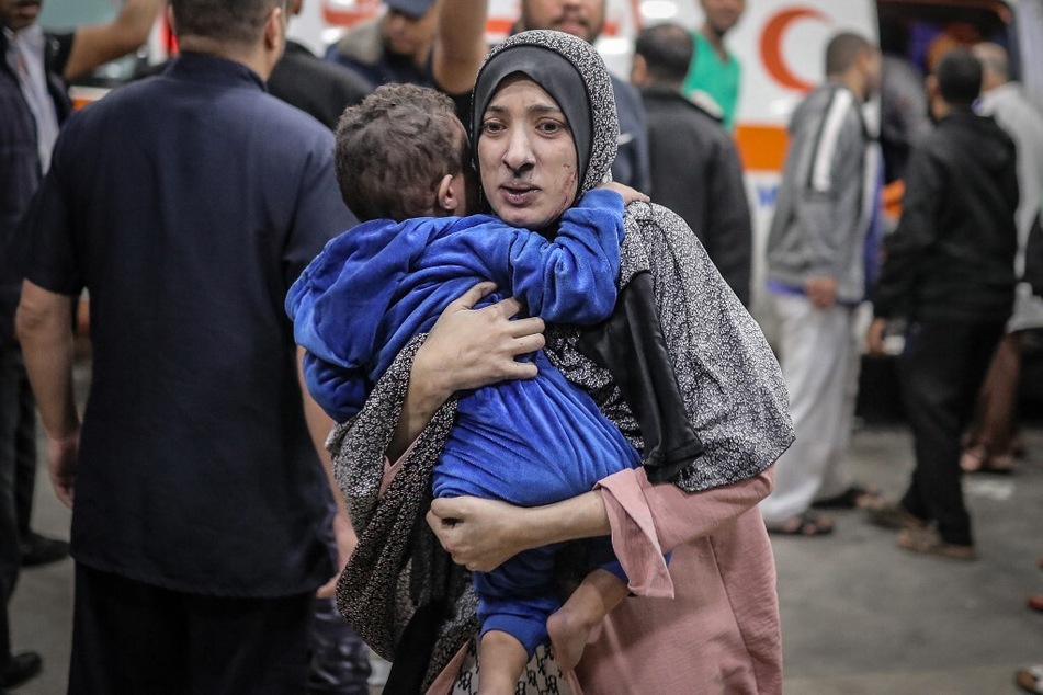 A Palestinian woman covered in dust rushes with her child in her arms into the hospital following the Israeli bombardment of Khan Younis in the southern Gaza Strip.