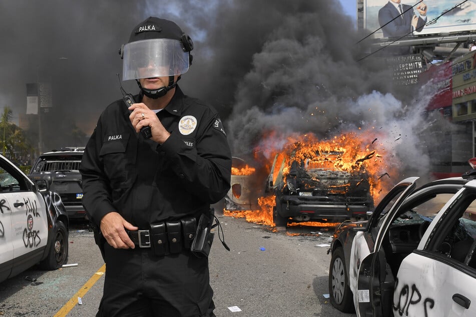 Los Angeles: Ein Kommandeur des Los Angeles Police Department, steht während eines Protests zwischen mehreren zerstörten, in Flammen stehenden Polizeiautos.