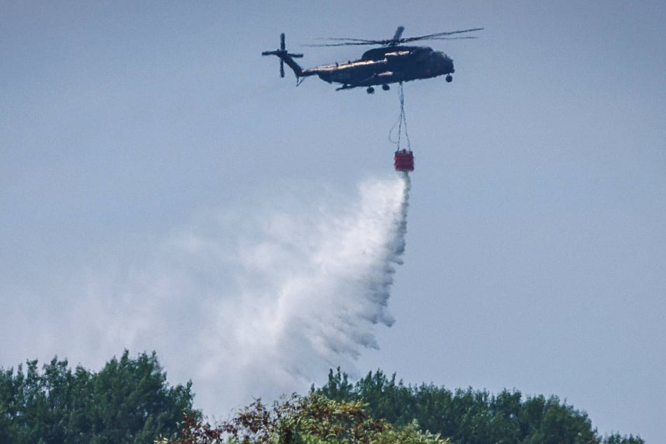 Hubschrauber der Bundeswehr werfen Wasser über dem Brandort ab.