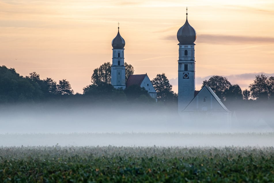 Morgennebel liegt vor der Wallfahrtskirche Mariä Himmelfahrt (r.) und der Kreuzkirche in Haindling. Marias – angebliche – Aufnahme in den Himmel spaltet Bayern.