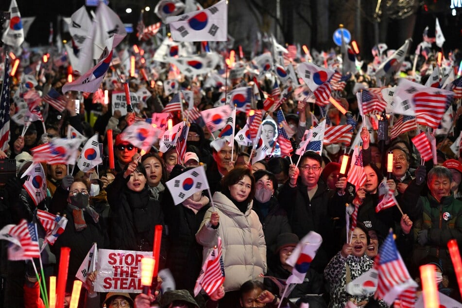 Supporters of impeached South Korean President Yoon Suk Yeol wave South Korean and US flags during a rally near the presidential residence in Seoul on Saturday after a motorcade carrying Yoon arrived at the residence.