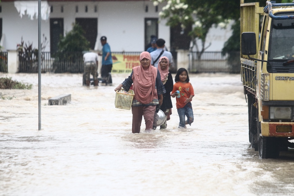 Anwohnerinnen waten nach einer Sturzflut mit ihren Habseligkeiten durch das Wasser auf einer überschwemmten Straße in der Provinz Süd-Sulawesi.