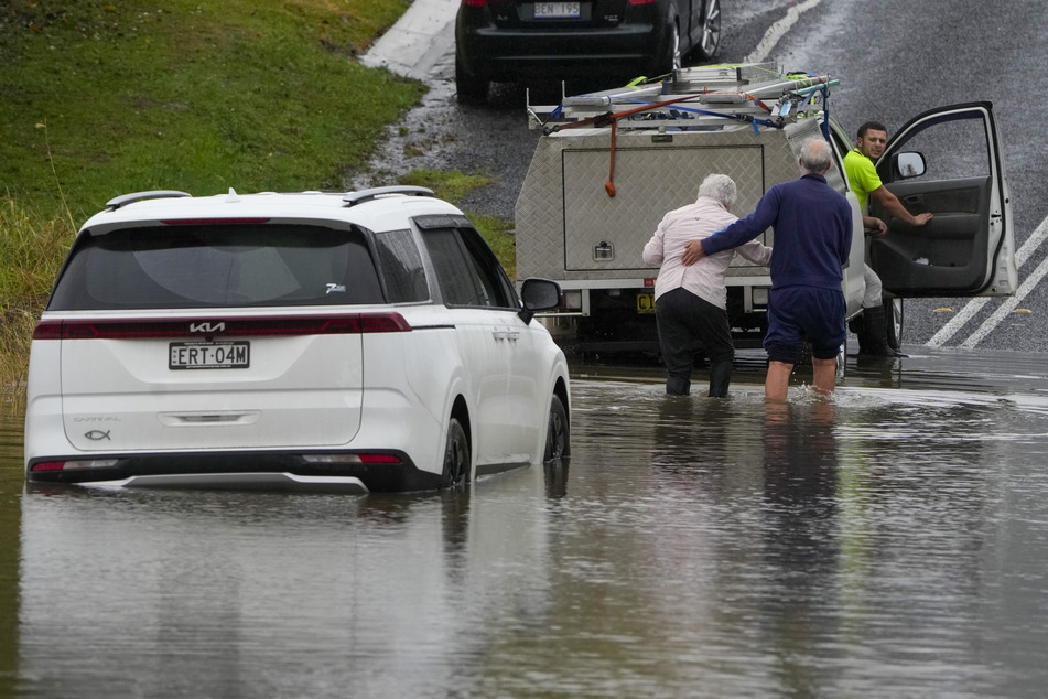 Eine Frau und ein Mann steigen am Stadtrand von Sydney aus ihrem im Hochwasser stehenden Auto.