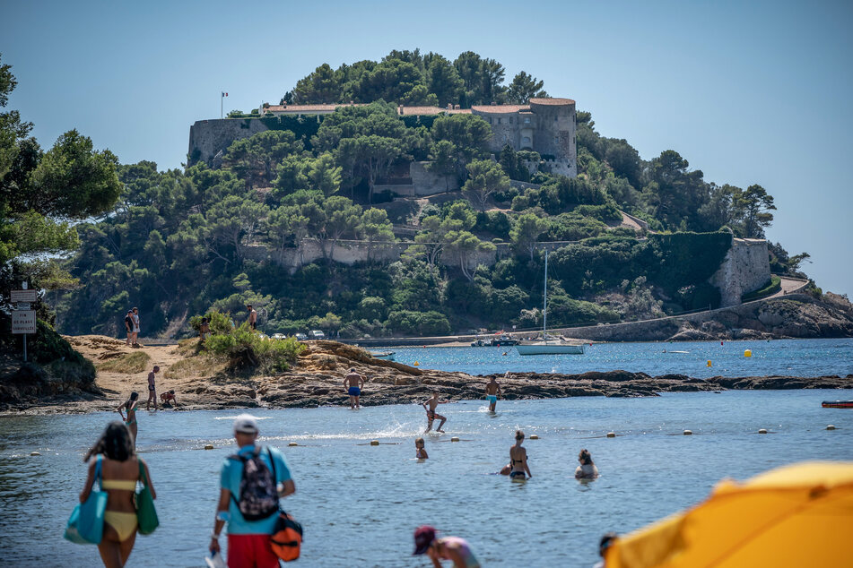Frankreich, Bormes-Les-Mimosas: Badegäste schwimmen unterhalb der Sommerresidenz des Staatschefs von Frankreich, Macron, dem Fort de Bregancon am Mittelmeer.