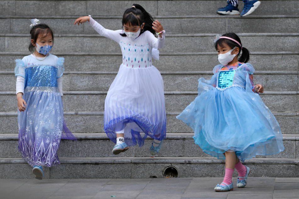 Mädchen in Prinzessinnenkleidern spielen auf einer Treppe und tragen dabei Masken gegen das Coronavirus.