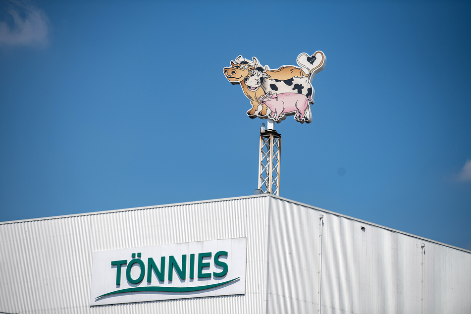Auf dem Dach eines Gebäudes auf dem Werksgelände steht das Logo der Firma Tönnies in Form von zwei Kühen und einem Schwein.