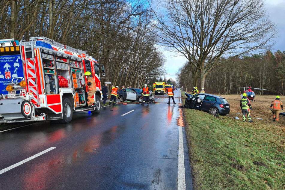 Das Foto zeigt das Unfallgeschehen: Links im Bild ist der Audi zu sehen, rechts der Skoda. Auf dem Feld neben der Landstraße steht ein Rettungshubschrauber zum Abtransport eines Schwerverletzten bereit. Auf der Straße und dem Feld liegen überall Fahrzeugteile.