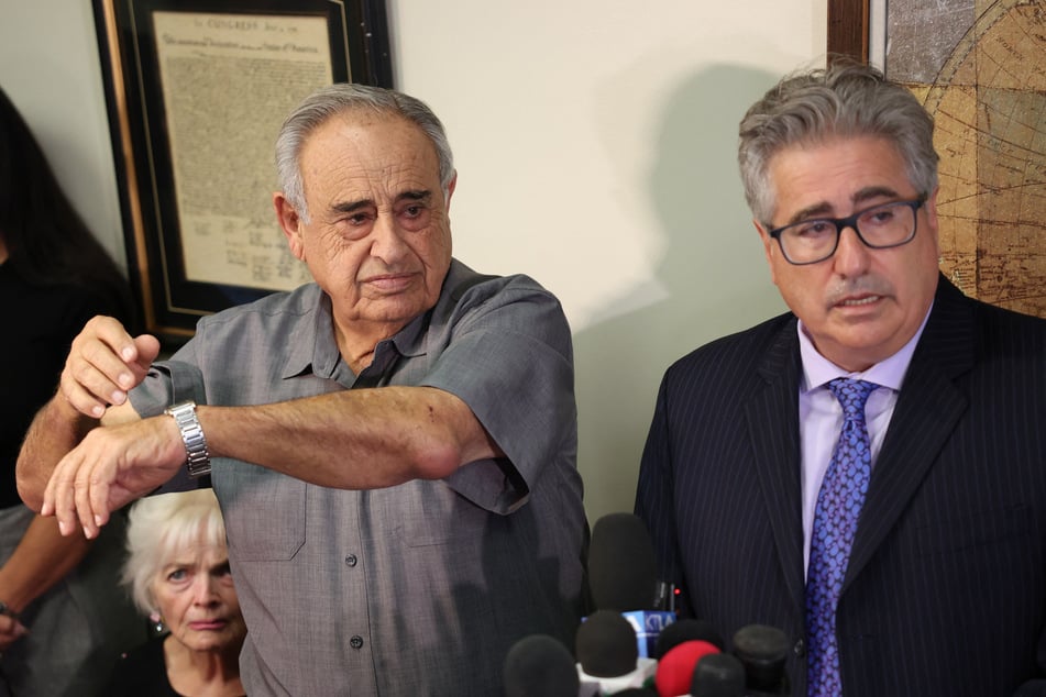 Car wash owner Rafie Ollah Shouhed lifts his elbow to show injuries received while speaking alongside his attorney V. James DeSimone at a press conference in Los Angeles, California, on September 25, 2025.