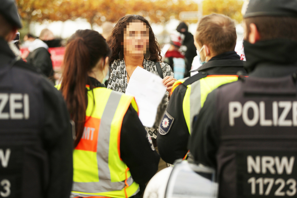 Eine junge Frau mit einem ärztlichen Attest, das sie vom Tragen eines Mund-Nasen-Schutzes freistellt, wird von der Polizei kontrolliert.