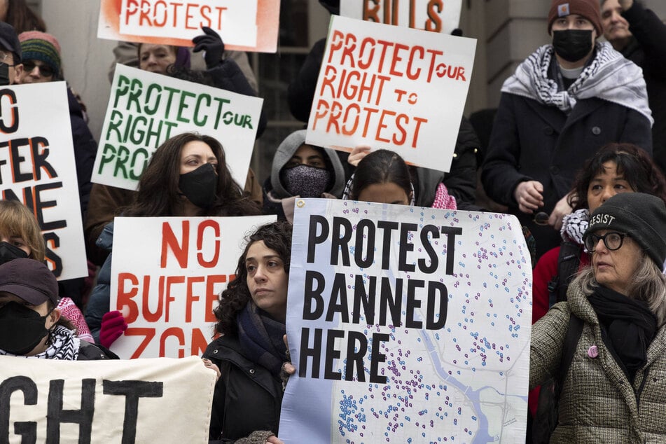 Attendees at a rally outside New York City Hall hold signs reading "Protest Banned Here" with a map of Manhattan and The Bronx and "Protect Our Right to Protest" on February 25, 2026.