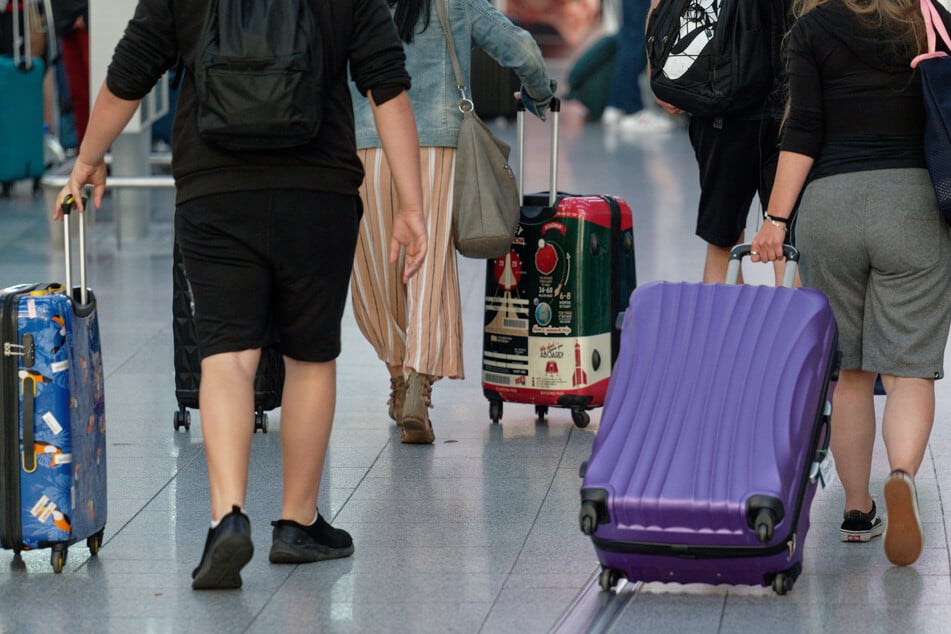 Reisende gehen in einem Flughafen mit Koffern durch die Abflughalle.