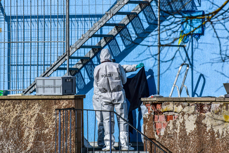 Polizisten stehen bei der Spurensicherung an der Rückseite eines blauen Wohn- und Geschäftshauses - der mutmaßliche Tatort.