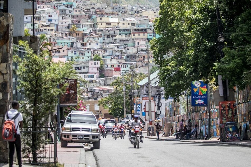 Traffic makes its way through a street in the Haitian capital of Port-au-Prince, with the slum of Jalousie in the background.