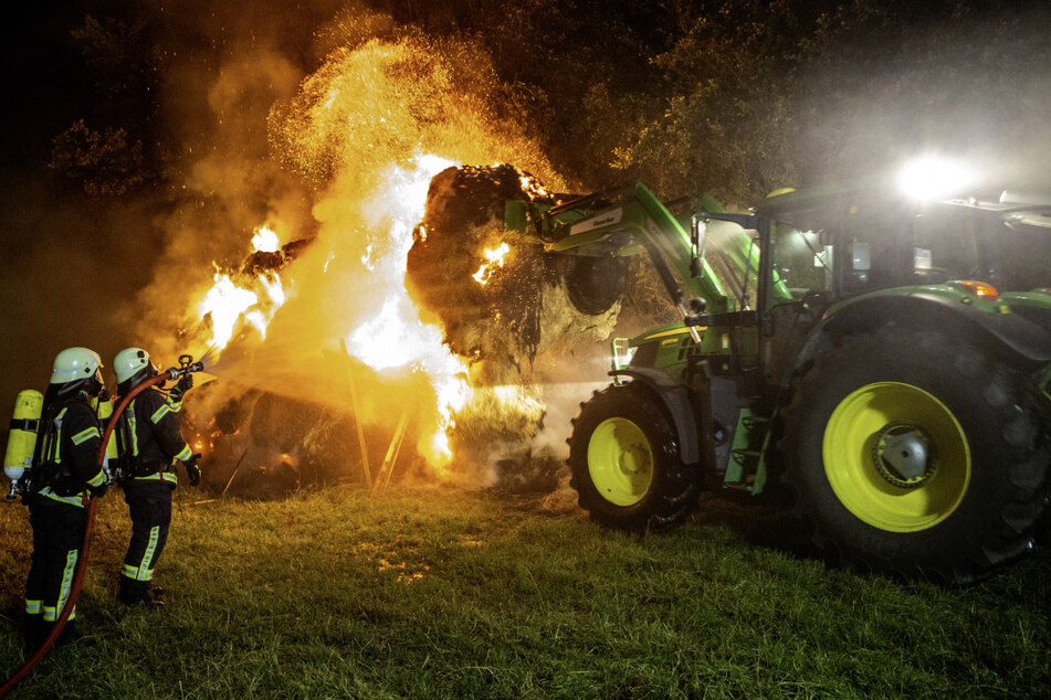 Mithilfe eines Traktors zieht ein Landwirt die brennenden Heuballen auseinander, damit sie besser gelöscht werden können.
