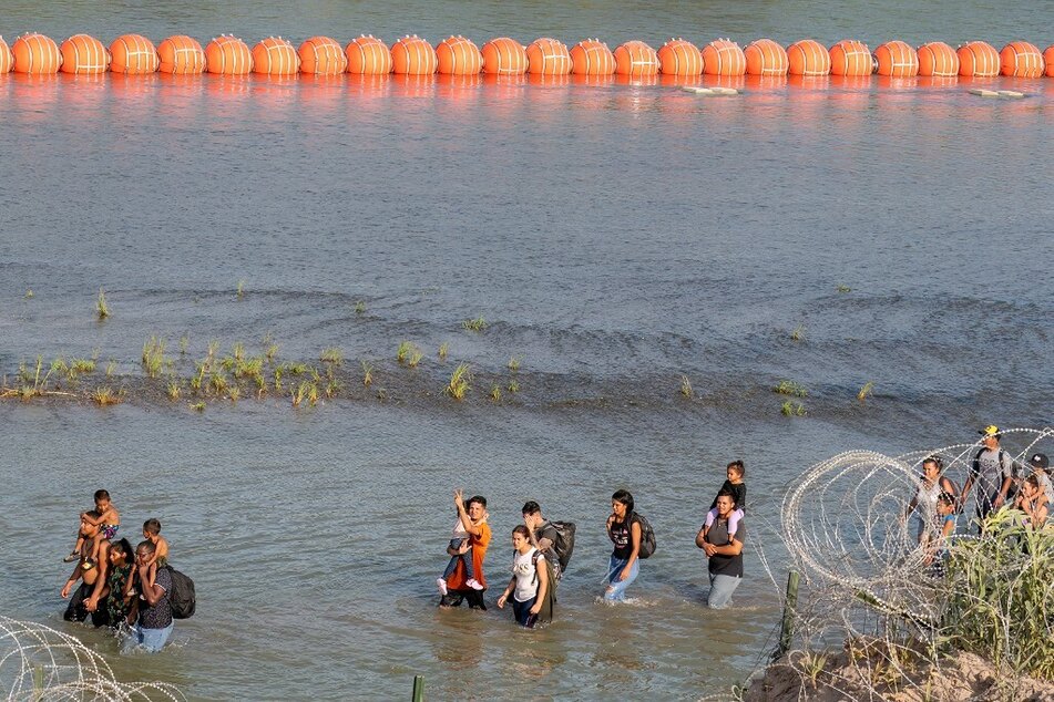 Migrants walk between razor wire and a string of buoys in the water along the Rio Grande border with Mexico in Eagle Pass, Texas.