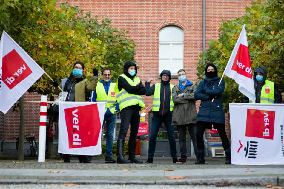 Teilnehmer eines Warnstreiks von Beschäftigten der Berliner Charité stehen auf dem Campus Charité Mitte mit Verdi-Fahnen für ein Foto zusammen.
