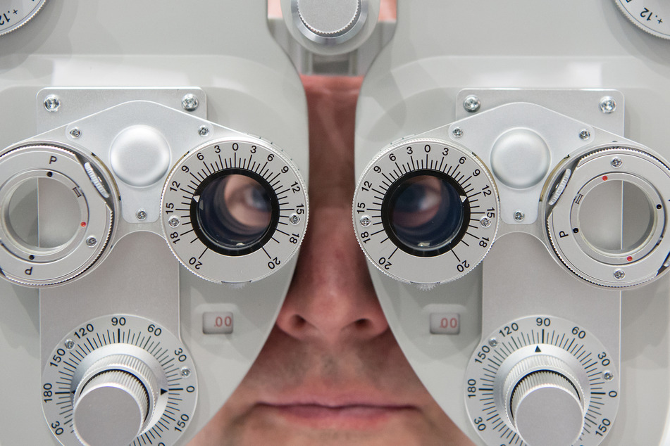Ein Mann sitzt auf der Optik- und Brillenmesse Opti hinter einem Phoropter, einem augenoptischen Gerät zur Ermittung von Fehlsichtigkeiten und zur Anpassung von Brillengläsern.