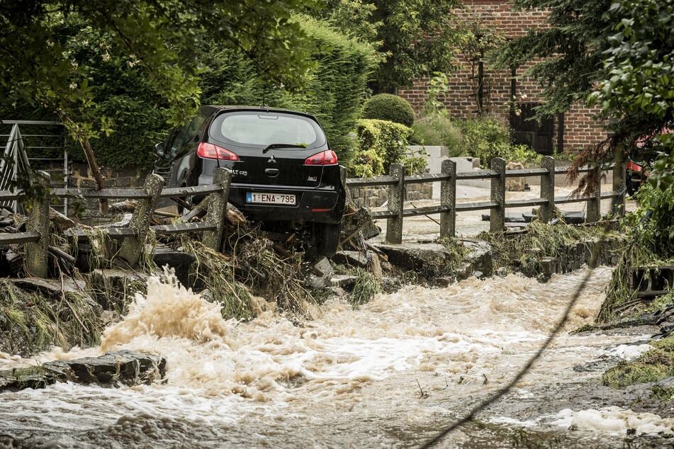 Ein Auto wird von den Wassermassen auf einer überfluteten Straße durch einen Zaun mitgerissen. Teile von Belgien wurden von starken Regenfällen heimgesucht.