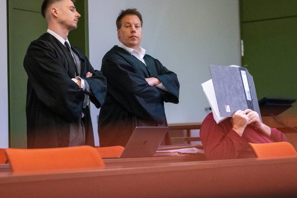 Der 77-jährige Angeklagter (r.) sitzt zum Prozess-Auftakt bei seinen Verteidigern in einem Sitzungssaal im Landgericht München.