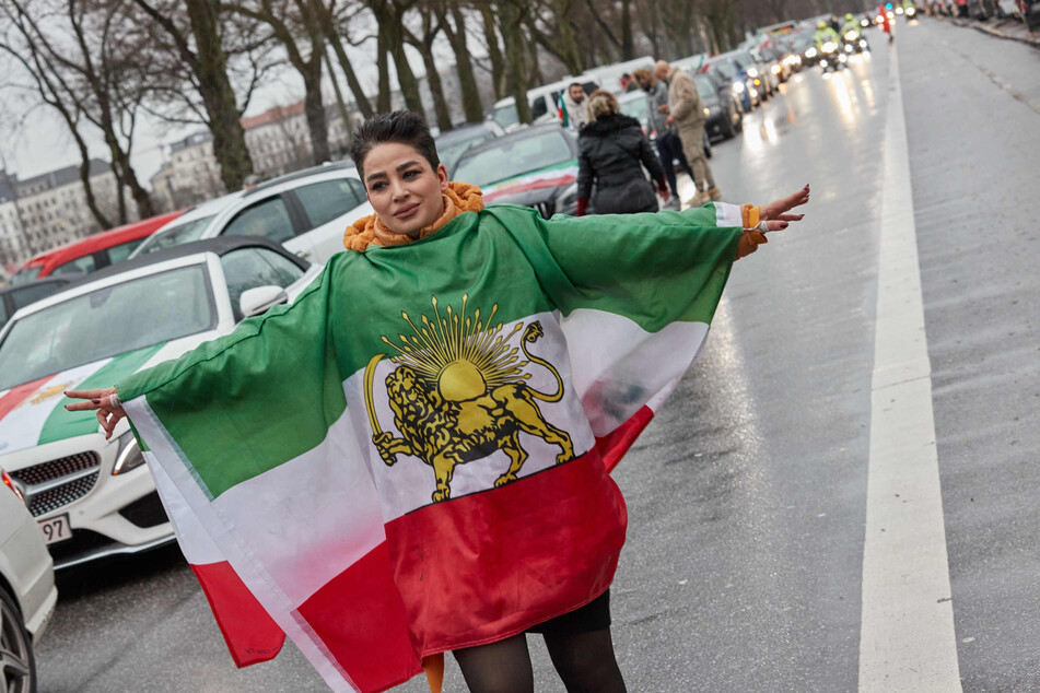 Eine Teilnehmerin der Auto-Demo trägt eine historische Flagge des Irans
