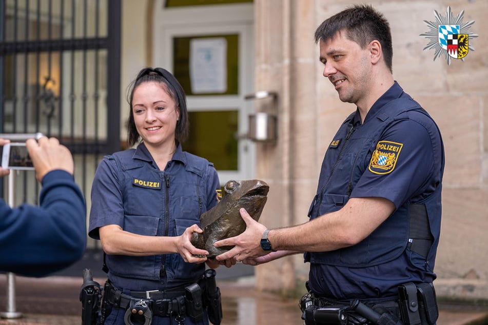 Eine Polizistin und ein Polizist halten den wiedergefundenen Bronzefrosch aus dem Stadtpark Nürnberg in den Händen.
