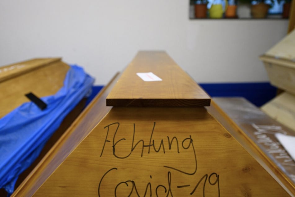 "Achtung Covid-19" steht auf einem Sarg mit einem Verstorbenen, der an oder mit dem Coronavirus gestorben ist, welcher im Krematorium in der Kühlung steht.