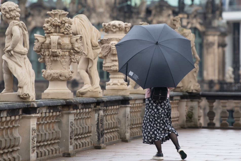 Mit Regenschirm ist eine junge Frau im Zwinger unterwegs.