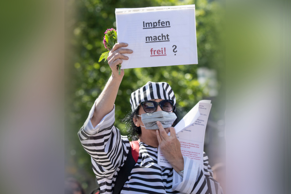 Ein Frau steht in einem Häftlingskostüm mit einem Schild «Impfen macht frei ?» bei einer Kundgebung gegen die Corona-Maßnahmen der Regierung.