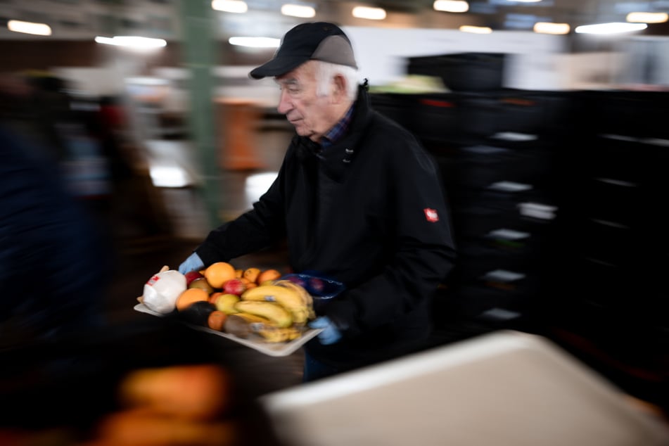 Ein Mitarbeiter der Oberhausener Tafel (NRW) trägt ein Tablett mit Obst.