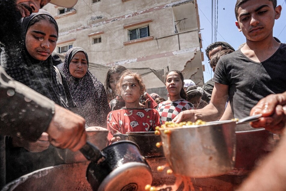 People are handed out food portions from a large pot at a public kitchen in Deir el-Balah in the central Gaza Strip.