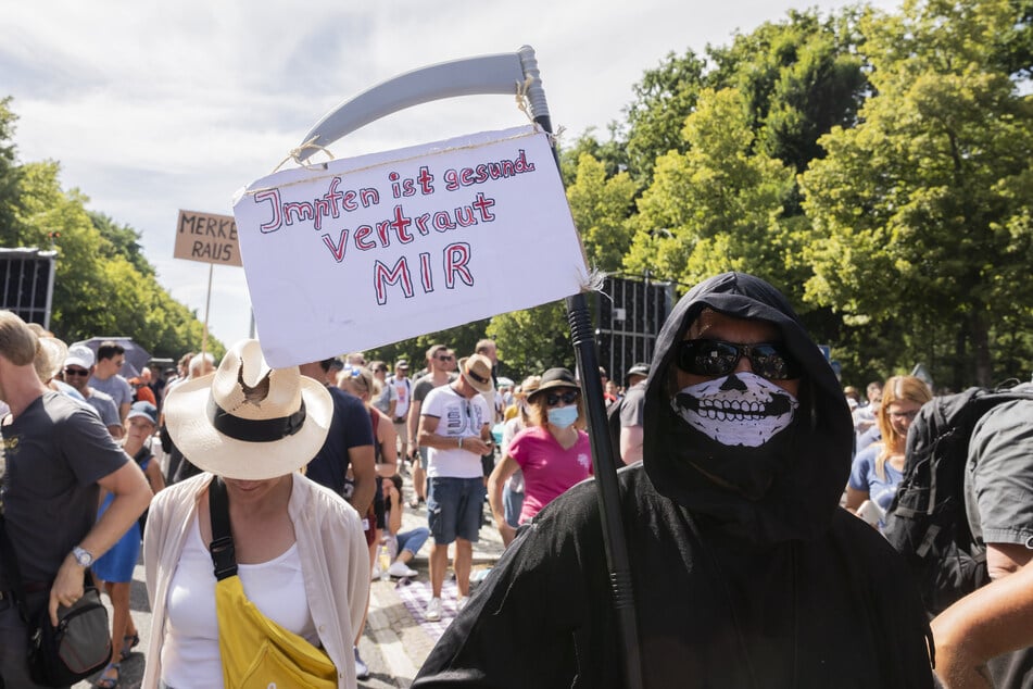 Eine Person im Sensenmann-Kostüm hält bei der Kundgebung gegen die Corona-Beschränkungen auf der Straße des 17. Juni ein Schild mit der Aufschrift "Impfen ist gesund, vertraut mir".