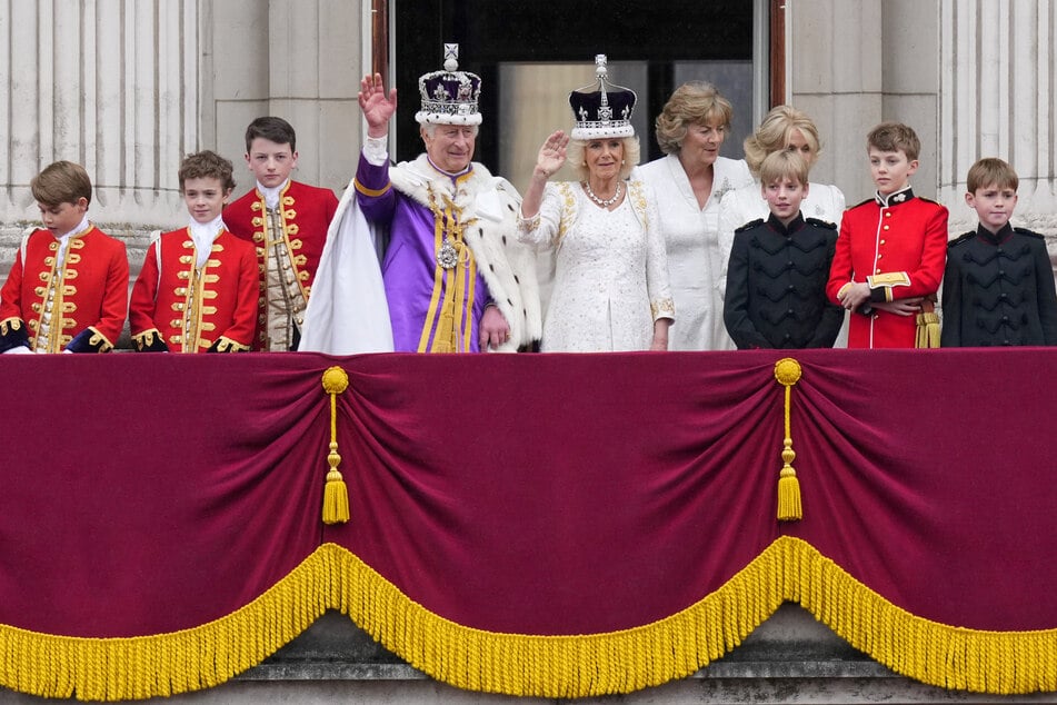 König Charles III. (M,l) und Königin Camilla (M,r) winken nach ihrer Krönungszeremonie vom Balkon des Buckingham Palastes aus der Menge zu.