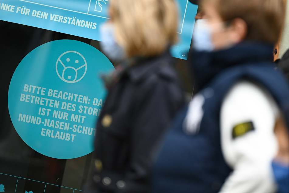Passanten, die einen Mund-Nasen-Schutz tragen, gehen auf der Frankfurter Zeil an einem Hinweisschild vorbei.