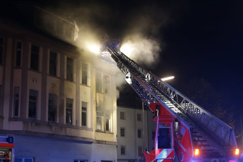 Feuerwehrkräfte versuchen mithilfe einer Feuerwehrleiter einen Brand in einem Mehrfamilienhaus zu löschen.