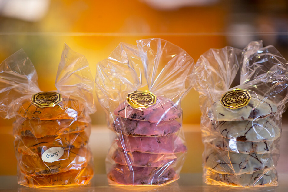 Drei Packungen Lebkuchen mit einem Überzug von Orangenschokolade (l), Erdbeerschokolade (M) und weißer Schokolade stehen in der Lebküchnerei Düll, auf der Theke.