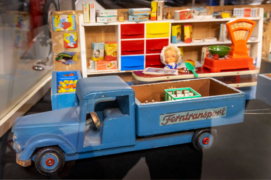 In einer Vitrine ist ein kleines Holz-Lieferfahrzeug und ein Kaufmannsladen zu sehen.