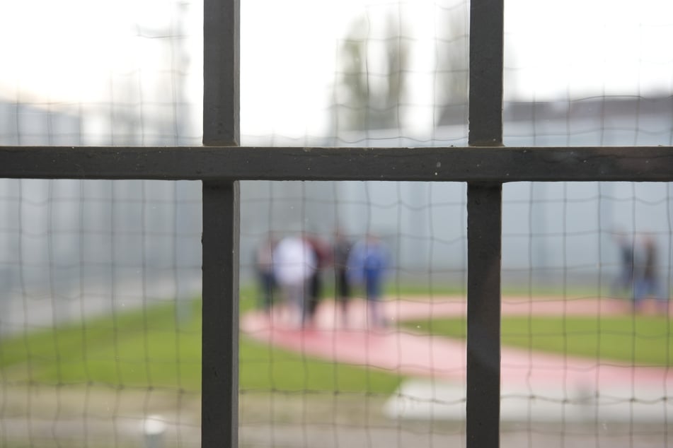 Hinter einem Gitter laufen Gefängnisinsassen einer Justizvollzugsanstalt über einen Gefängnishof. (Symbolbild)
