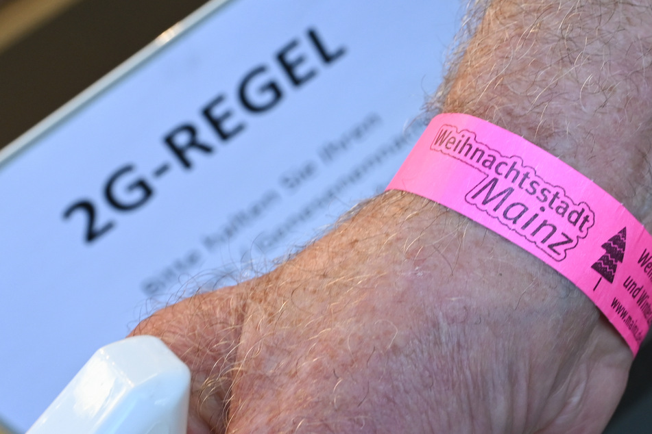 Ein Mann hält seinen Arm mit einem 2G-Bändchen am Eingang eines Modegeschäfts in der Mainzer Innenstadt vor ein Schild mit der Aufschrift "2G-Regel".