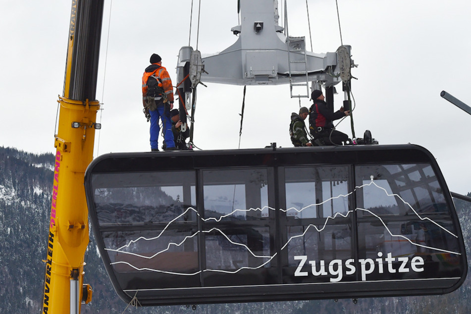 Arbeiter sitzen auf der Gondel der Zuspitzbahn. Auf Deutschlands höchstem Berg soll nun ein Lift ersetzt und ein Skitunnel gebaut werden.